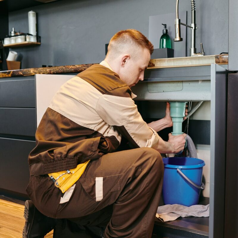 Modern plumber in workwear changing pipe under sink